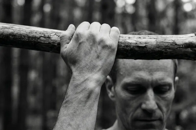 Eine intime Nahaufnahme der Hand eines Athleten, die einen rauen Baumstamm greift, symbolisiert die ununterbrochene Aufmerksamkeit und die Verbindung zwischen Geist und Muskel beim regelmäßigen Sport treiben.