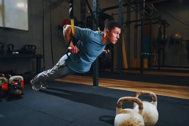 Ein Mann macht Liegestütze an einem Schlingentrainer im Fitnessstudio. 