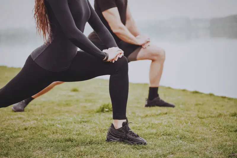 Eine Frau und ein Mann dehnen sich nach dem Lauf an einem See.