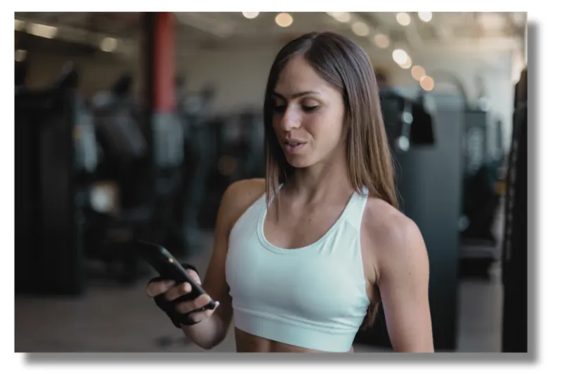 Eine junge Frau schaut während des Trainings im Fitnessstudio auf ihr Handy.